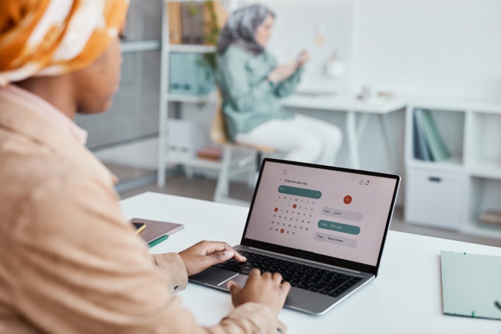 Young woman wearing a brown scarf and beige shirt using a tablet with a calendar on the display.