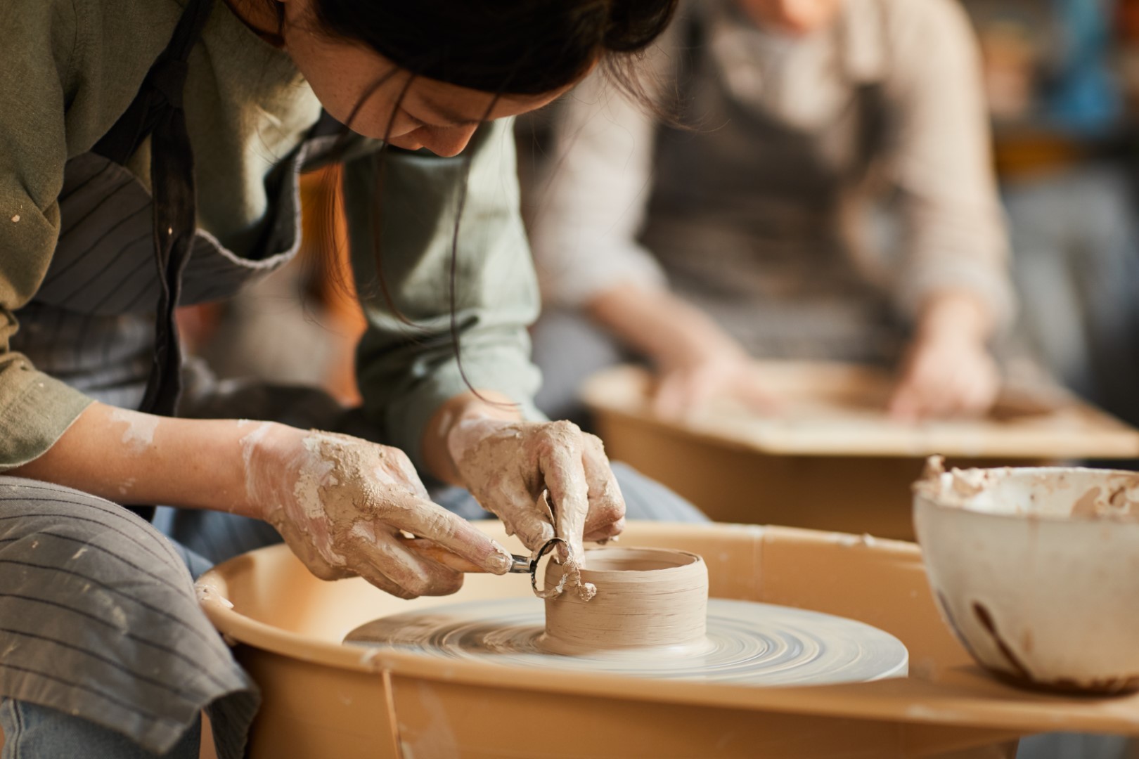 A young woman using a pottery wheel looking down