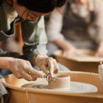 A young woman using a pottery wheel looking down